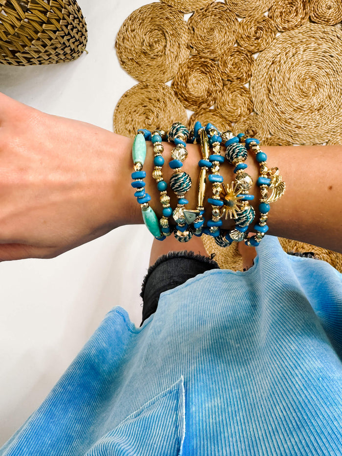 Blue Set of Nine Beaded Stretch Bracelets Featuring Gold Tones And Metallic Rope Wrapped Beads With Wing & Sun Charms