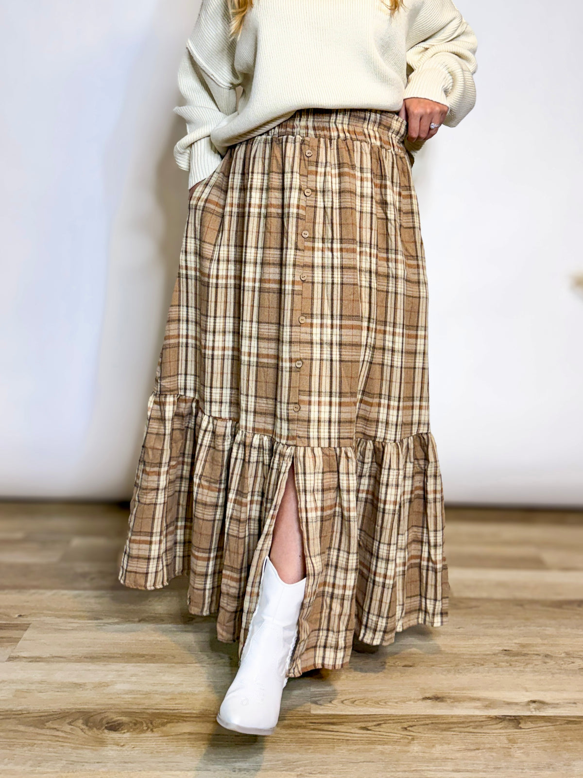 A long brown and beige plaid skirt with a button front and ruffled hem, paired with a cream sweater and white cowboy boots