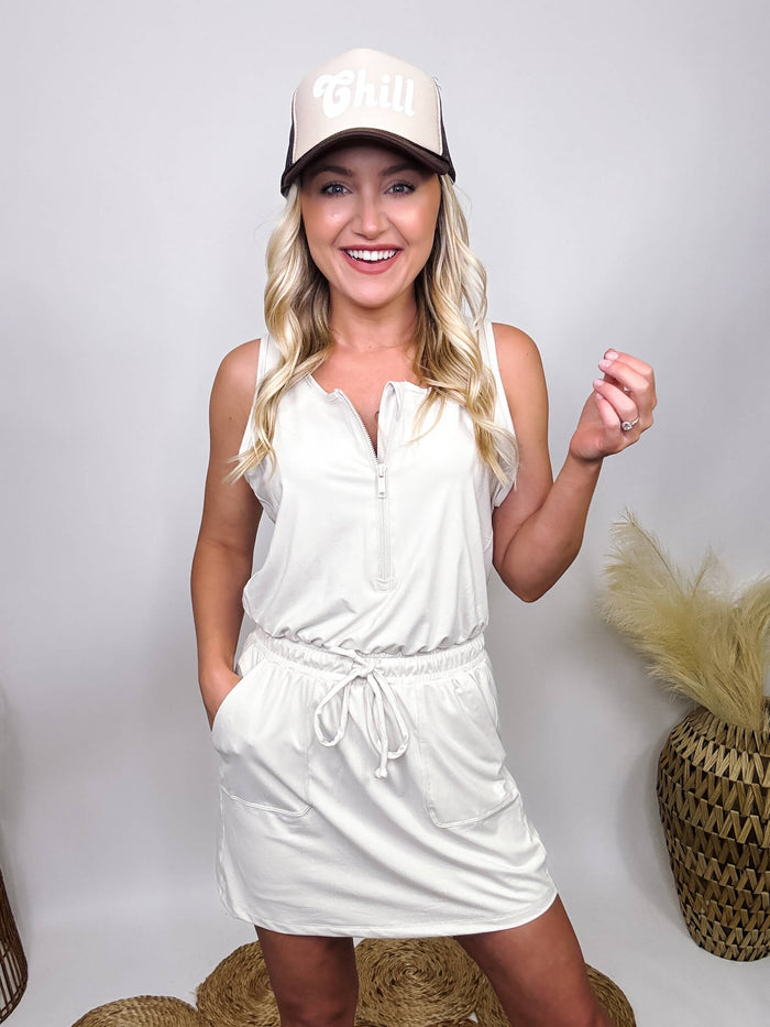 Rae Mode White Pearl Romper Dress with Built-in Biker Shorts, Elastic Drawstring Waist, Functioning Zipper, Side Pockets, and Stretchy Buttery Soft Material. Styled with a 'Chill' Trucker Hat