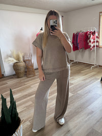 A woman’s matching two-piece lounge set consisting of a short-sleeve crewneck top and wide-leg pants in a heathered taupe color.