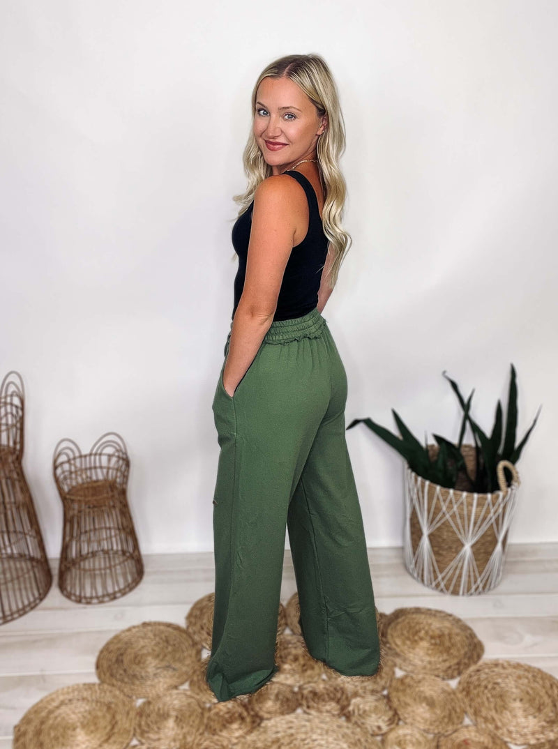 Image of Zenana brand Ash Green French Terry Wide Leg Pants. The pants feature a laser cut design, an elastic drawstring waistband, and pockets. They have an oversized fit and are made of 100% cotton. The inseam is approximately 31.5 inches.