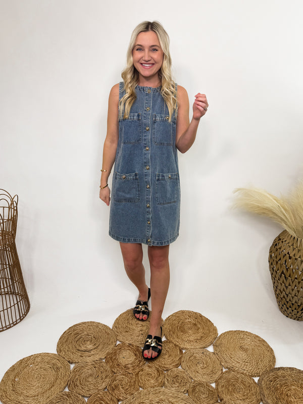 Sleeveless denim mini dress with a gold-colored button-down front, functional pockets, and a relaxed fit—perfect for spring and summer styling.