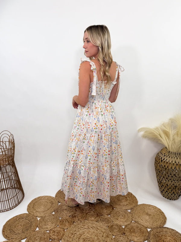 Wildflower Tiered Smocked Maxi Dress with Self Tying Straps – White with watercolor wildflower prints, smocked stretchy top, tiered flowy skirt, self-tie adjustable straps, side pockets, and fully lined. Perfect for spring and summer occasions like Easter, garden picnics, and baby showers. Flattering and boho-chic.
