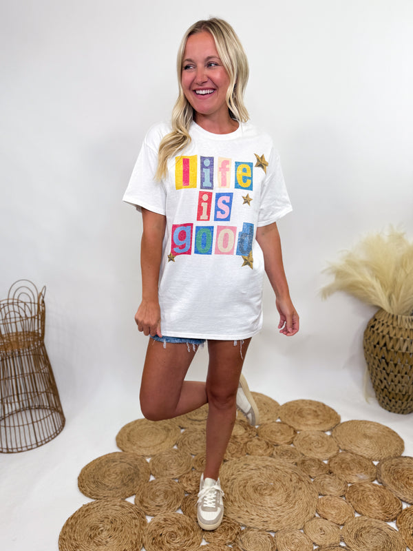 White oversized t-shirt with colorful “Life is Good” block lettering and stars