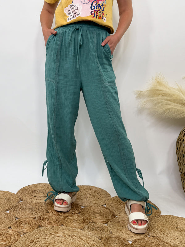 Sage green boho harem jogger pants with lace trim and adjustable side ties, styled with graphic tee