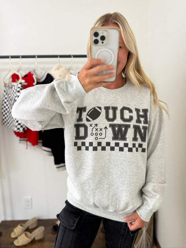 Heather gray graphic sweatshirt with “TOUCHDOWN” design featuring football and playbook print. Touchdown sweatshirt styled with black cargo jeans, perfect for game day. Cozy fleece-lined football sweatshirt with checker print detail. Oversized relaxed fit graphic sweatshirt for fall and football season