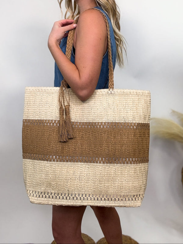 Two-tone woven tote bag with tassel detail, spacious and lightweight, perfect for beach vacations and everyday wear.